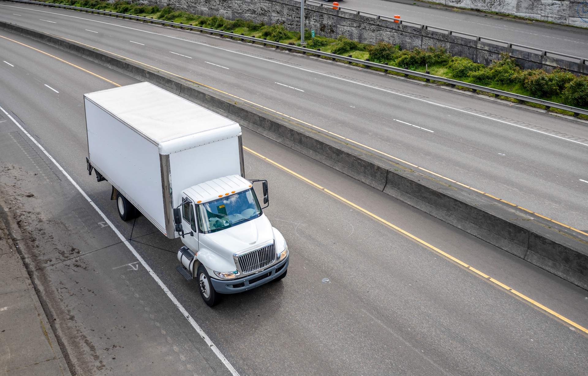 Powerful compact meddle size rig semi truck with box trailer driving on the highway road with exit intersection